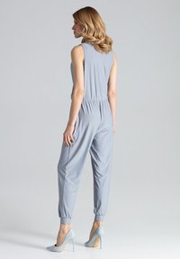 Lichtgrijze jumpsuit met een aansluitend lijfje, elastische tailleband en tapered benen. Gladde stof; gecombineerd met lichtblauwe hoge hakken.