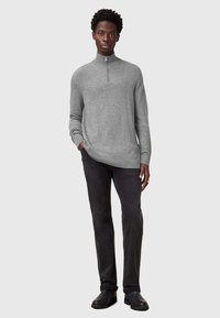 Pullover grigio a maniche lunghe con zip a un quarto e una vestibilità rilassata, abbinato a jeans scuri e scarpe slip-on nere. Tessuto semplice e testurizzato.