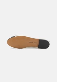 Semelle de chaussure blanche avec caoutchouc marron et accent noir. Présente une surface lisse et une légère texture pour l'adhérence. Logo imprimé au bas.