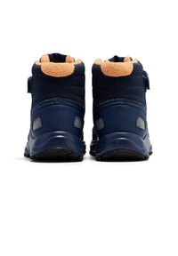 Zapatillas de caña alta en azul marino con un upper de tela texturizada, cuello de forro polar en contraste marrón y correa de velcro. Suela de goma con ranuras de tracción.