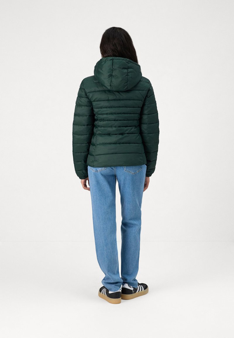 Groene pufferjack met een capuchon, gewatteerd ontwerp en geribbelde manchetten. Gecombineerd met lichtblauwe straight-leg jeans en zwarte sneakers.