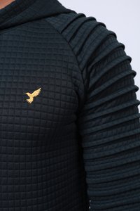 Hanorac matlasat de culoare verde închis, cu mâneci ribbate și un mic logo a unei păsări aurii pe piept. Textură moale cu un design structurat.
