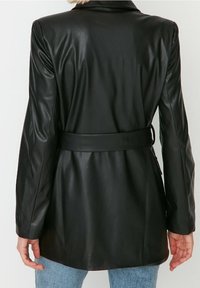 Zwarte leren blazer met een getailleerd ontwerp, lange mouwen en een tailleband; gladde textuur met minimale details en een klassieke kraag.