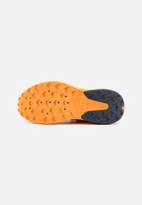 Terrengløpesko såle med et to-farget design, med en oransje gummibase og et svart teksturert mønster for grep og trekkraft.