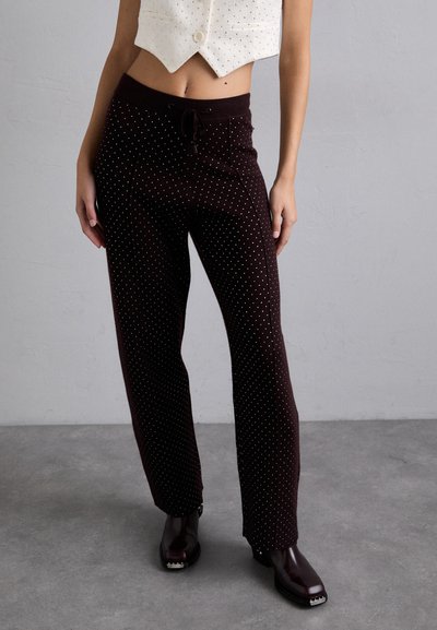 Pantaloni marroni con pois, dotati di una vita con cordoncino e un design a gamba dritta, realizzati in un tessuto morbido. Abbinati a scarpe marroni scure.