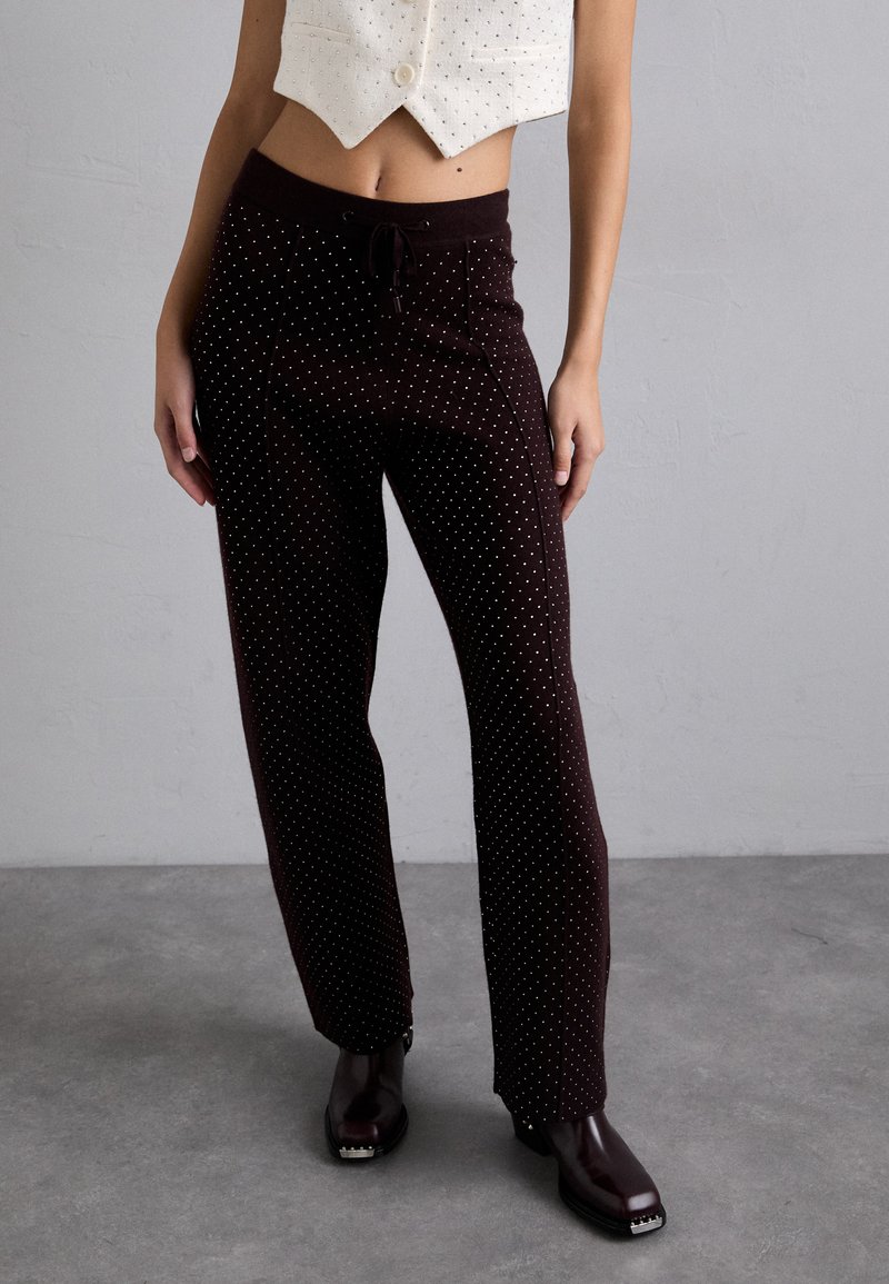 Bruine polkadot broek met een elastische tailleband en recht omhoog lopende pijpen, gemaakt van een zachte stof. Gecombineerd met donkerbruine schoenen.