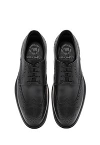 Chaussures de ville en cuir noir avec perforations en aile et lacets, vues du dessus sur un fond blanc.