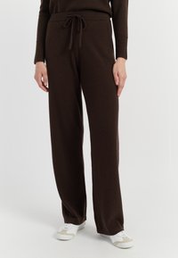 Bruine, ruime broek van zacht materiaal, met een trekkoord in de taille en rechte pijpen, gecombineerd met witte en beige sneakers.