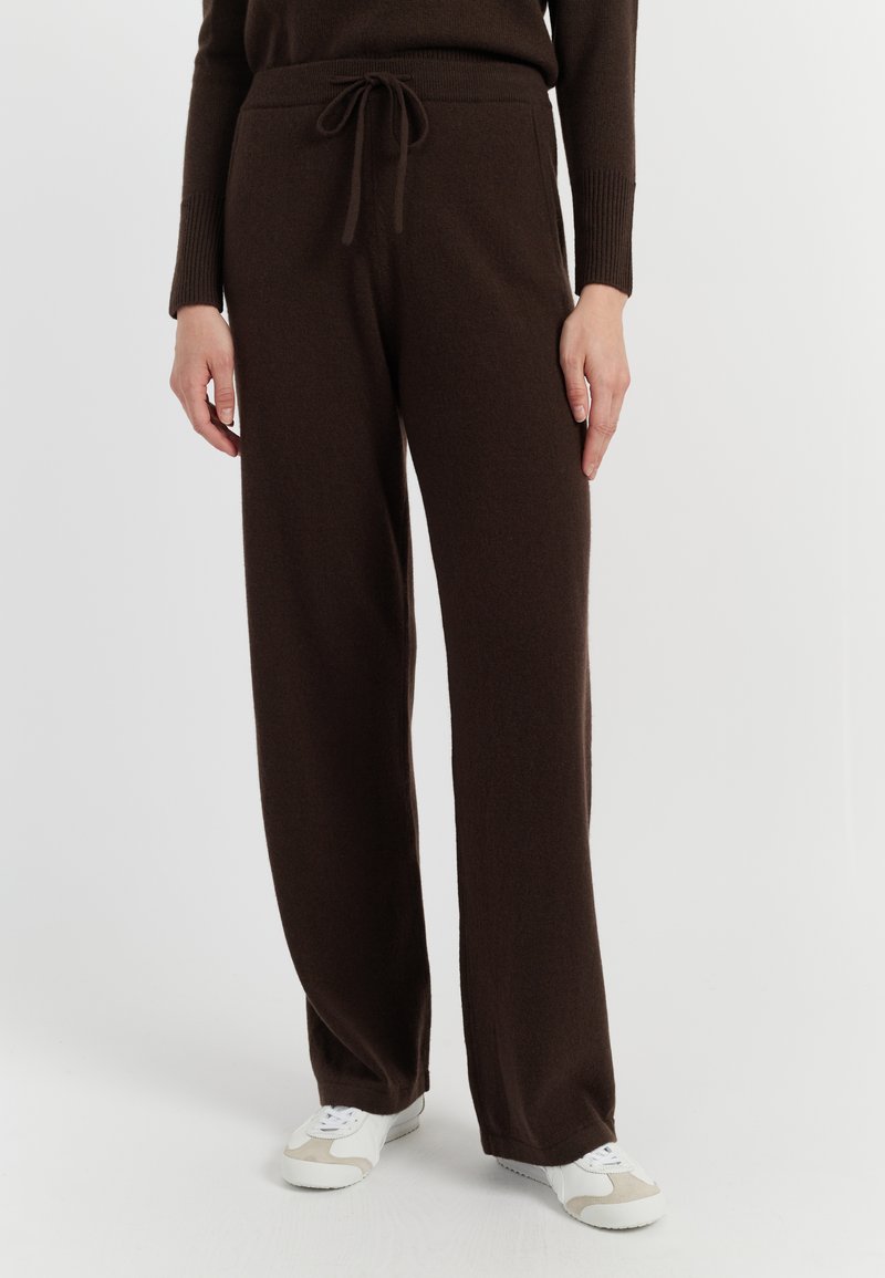 Bruine, ruime broek van zacht materiaal, met een trekkoord in de taille en rechte pijpen, gecombineerd met witte en beige sneakers.