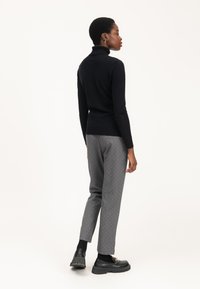 Maglione a collo alto nero abbinato a pantaloni grigi con piccoli pois bianchi. Modello che indossa scarpe nere con suola spessa.