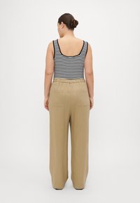 Top in tessuto a righe bianche e nere, abbinato a pantaloni larghi beige chiaro con vita con cordino e tasche posteriori.