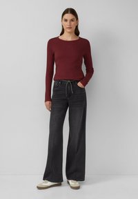 Rotes, figurbetontes Langarmoberteil, dunkle, weit geschnittene Jeans mit Kordelzug und weiße Sneaker. Glatte Textur mit dezenten Nahtdetails.