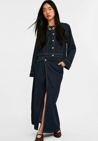 Donkerdenimjas en maxi-jurk set met een voorkleef, met zilveren knopen, contrasterende stiksels en een gestructureerd ontwerp.