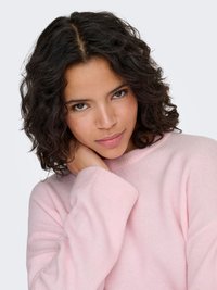 Jasnoróżowy, oversize'owy sweter o miękkiej fakturze i prążkowanych mankietach. Model ma okrągły dekolt i luźny fason.