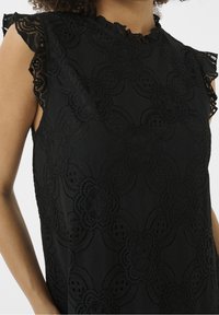 Černý krajkový top s květinovými vzory, rýhovanými okraji rukávů a texturovanou tkaninou. Design spojuje jemné detaily a hladký povrch.