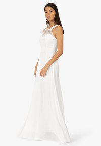 Witte vloerlange jurk met een aansluitend lijfje met kantdetails en een transparante overlay. Soepele stof met een vloeiende silhouet.