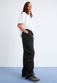 Weißes kurzärmliges T-Shirt kombiniert mit lockeren schwarzen Cargo-Hosen, die seitliche Taschen und eine entspannte Passform aufweisen, ergänzt durch gemusterte Sneaker.