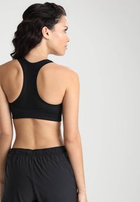 Crni sportski crop top s racerback dizajnom, izrađen od glatkog, rastezljivog materijala s detaljima od prozračne mreže.