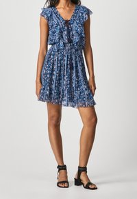 Sininen kukkamekko, jossa on röyhelöhuulet, vyötärö puristettu ja kellotettu hame. Yhdistetty mustiin niitatuilla korkokenkillä.