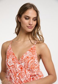 Rochie cu un model floral roșu și alb, cu decolteu în V adânc și bretele subțiri; material ușor, cu o textură netedă.