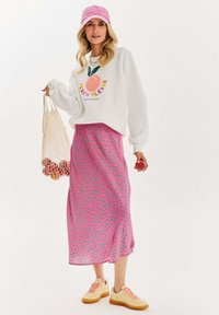 Bílá mikina s textem "Peach Please", růžová midi sukně s puntíky, žluté tenisky a růžová kšiltovka. Síťovaná taška s pomeranči.