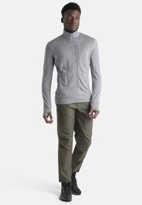 Gray zip-up jacket in a lightweight fabric, featuring a high collar and long sleeves. Paired with olive cargo pants and black boots.