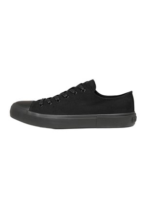 Zapatilla negra de lona de caña baja con suela de goma negra, puntera y cordones negros, mostrada de lado sobre un fondo blanco.