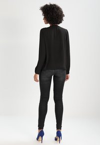 Blouse noire à manches longues avec un col rond, en tissu lisse, associée à un jean skinny sombre et des chaussures à talons hauts bleues. Design simple et épuré.