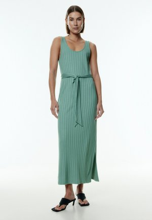 Mintgrünes, geripptes Maxikleid mit tailliertem Oberteil, Gürtel in der Taille und seitlichem Schlitz, kombiniert mit schwarzen, offen-toe High Heels.