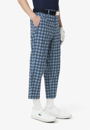 Blauwe geruite broek met een losse pasvorm, zichtbare zakken, elastische tailleband, en gecombineerd met witte sneakers en sokken.