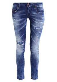 Hubené modré džíny vyrobené z denimu s opotřebovanými detaily, vybledlými oblastmi a několika výřezy. Mají zapínání na knoflík a zip a kapsy.