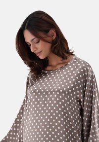 Blusa marrone a pois realizzata in tessuto liscio, con scollo ampio e maniche larghe, caratterizzata da motivi circolari bianchi distribuiti in modo uniforme.