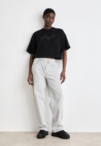 Musta lyhyt t-paita, jossa kirjailtu teksti, yhdistetty vaaleanharmaisiin leveälahkeisiin farkkuihin ja mustiin lenkkareihin. Minimalistinen muotoilu, pehmeä kangas.