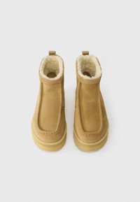 Tanen suedirane gležnjače s mekanym bijelim podstavom, okruglim vrhom i jednostavnim dizajnom. Imaju stražnju petlju za lako obuvanje i debeli svijetli đon.