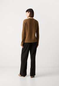 Bruine geribbelde gebreide sweater met een relaxte fit, voorzien van een textuurdesign en een uitlopende zoom, gecombineerd met zwarte wijde broek en beige hakken.