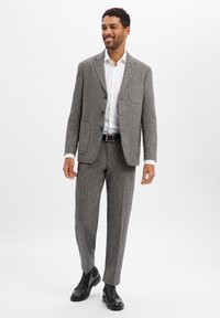 Szary garnitur w jodełkę z marynarką na dwa guziki, dopasowanymi zwężanymi spodniami i czarnymi butami. Ma kieszeń na piersi i gładką fakturę.