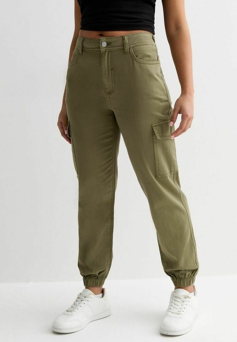 Olijfgroene cargo broek met taps toelopende enkelboorden en zijzakken, gemaakt van een gladde stof. Dragen met witte sneakers.