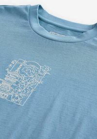 Svijetloplava pamučna majica s bijelim izvezenim dizajnom pagode i cvjetnim motivima na prednjem dijelu. Glatka tekstura, okrugli izrez.