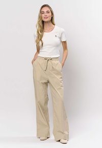 Valkoinen ribbineulottu lyhythihainen paita yhdistettynä vaaleanbeigeihin, korkeavyötäröisiin, väljälahkeisiin housuihin, joissa on vyösolki vyötäröllä ja sivutaskut.