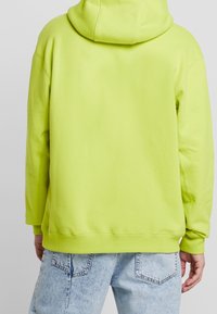 Světle zelená mikina s kapucí a uvolněným střihem. Hladká bavlněná textura, žebrované manžety a lem. Obsahuje zadní kapsu typu klokan.