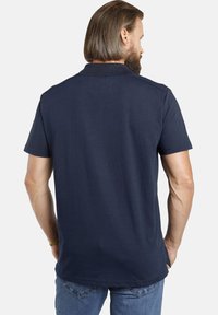 Dunkelblaues Kurzarm-Polohemd mit klassischem Kragen, Rückennähten und einem lockeren Schnitt, kombiniert mit hellblauen Jeans.