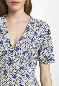 Floral Kleid aus weißem Stoff mit blauen Schmetterlingsmustern, V-Ausschnitt und kurzen Puffärmeln mit elastischen Bündchen.