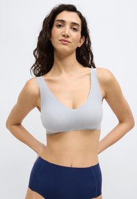 Ανοιχτό γκρι ασύρματο σουτιέν με V-λαιμόκοψη και φαρδιές τιράντες, με λείο ύφασμα και άνετο, αδιάκριτο σχέδιο χωρίς ραφές. Συνδυάζεται με σκούρα ναυτικά ψηλόμεσα κάτω μέρη.