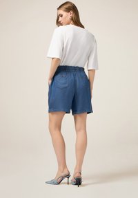 Shorts in denim con vestibilità rilassata, vita elasticizzata, tasche laterali e tasche posteriori cucite. Abbinati a una maglietta bianca a maniche corte.
