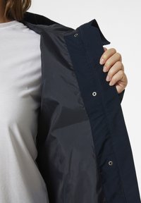 Chaqueta azul marino con un forro interior liso y brillante. Cuenta con broches a presión y un diseño de cuello clásico. El material parece ligero y duradero.