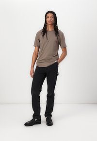 Braunes, kurzärmeliges T-Shirt mit lockerer Passform, kombiniert mit schwarzen Jeans. Schwarze Schuhe runden das lässige Outfit ab. Einfaches Design, einfarbige Farben.