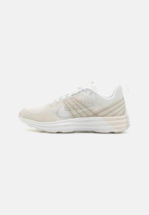 Chaussure de course légère en maille blanche et beige clair, dotée d'une semelle rembourrée, d'un design à lacets et de motifs de rayures subtils sur l'empeigne.