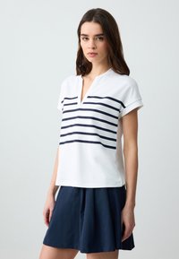 Weißes kurzärmeliges Oberteil mit navyfarbenen horizontalen Streifen, V-Ausschnitt-Design, kombiniert mit einem dunkelblauen ausgestellten Rock. Glatte Stofftextur.