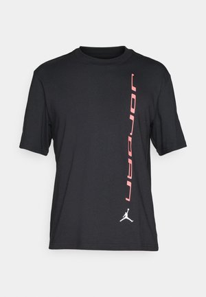 Sort kortærmet t-shirt lavet af bomuld; har lodret "JORDAN" tekst i pink og et hvidt Jumpman logo i nederste højre hjørne.