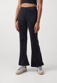 Black flared pants made of soft, stretchy fabric; features a smooth texture and a fitted waistline. Paired with light gray sneakers.